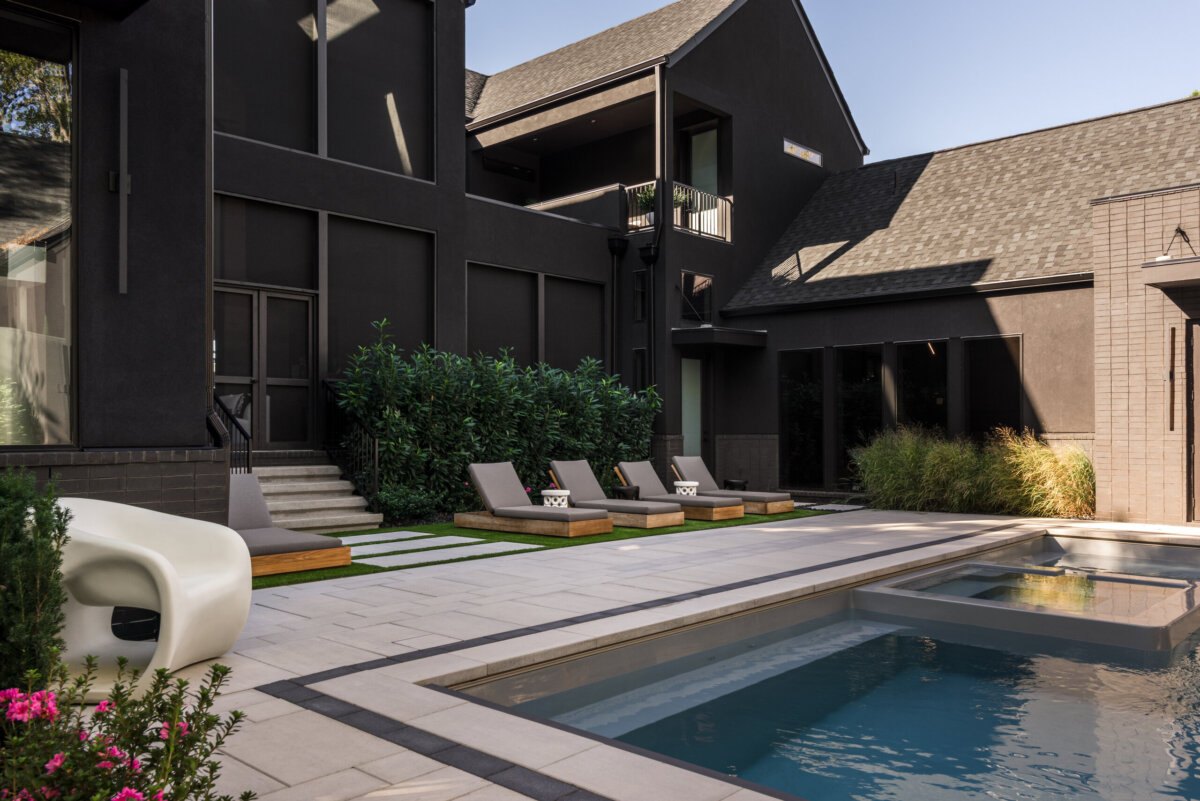 There's a Graffiti-Covered Bust in This Nashville Home, and It Works - 19 Striking modern backyard with a pool, spa, four lounge chairs on wooden decks, dark exterior house reminiscent of a Nashville home, lush greenery, and a slide visible on the left—creating an ambiance worthy of a modern art gallery.
