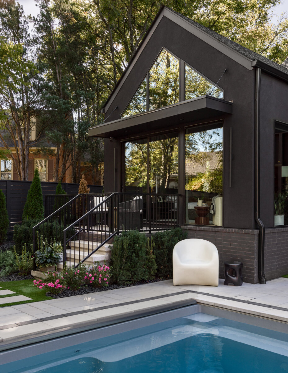 There's a Graffiti-Covered Bust in This Nashville Home, and It Works - 17 Modern black Nashville home with large windows overlooks a landscaped backyard featuring a swimming pool, white chair, stone tiles, and green shrubs. Striking in its design, this residence evokes the clean lines of a modern art gallery, while tall trees and fencing provide privacy.