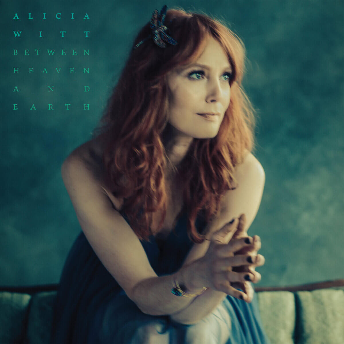 Alicia Witt Just Released Her Most Personal Album Yet - 4 Alicia Witt sits on a green couch, hands clasped, looking to the side. Text on the image reads "Alicia Witt Between Heaven and Earth.