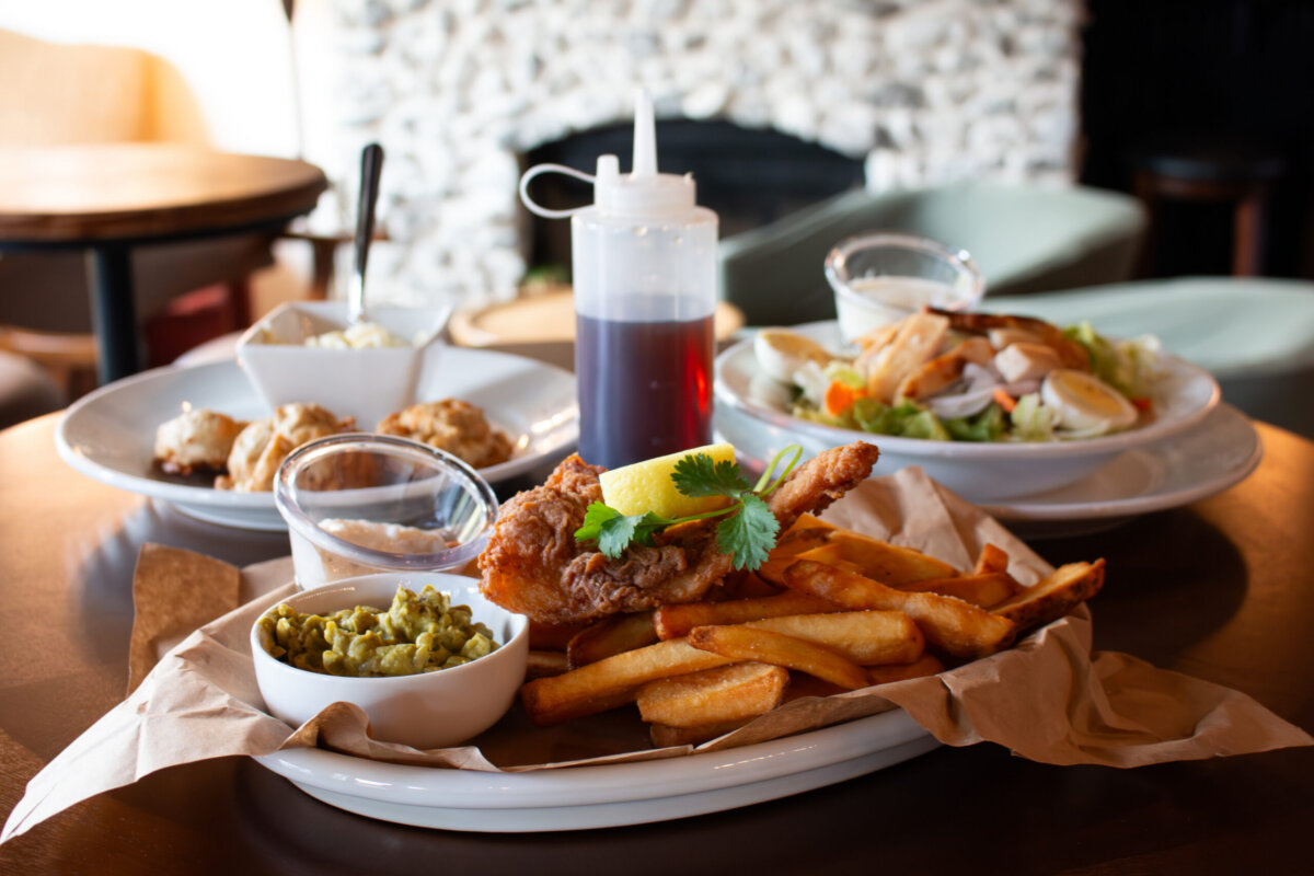 5 Destinations Where Southern Charm Thrives - 11 Plate of fried fish with fries, peas, and lemon garnish in the foreground; salad, biscuits, and sauce bottle in the background on a restaurant table.