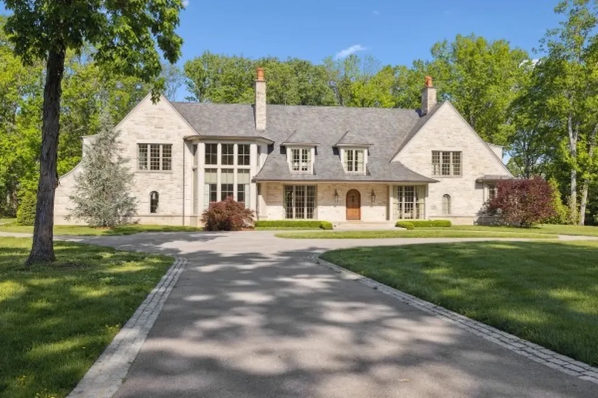 You’re About to Notice Chimney Pots Everywhere - 5 Large two-story stone house with multiple chimneys adorned with classic chimney pots, a steep roof, and an arched wooden front door, set amid green lawn and trees under a clear blue sky.