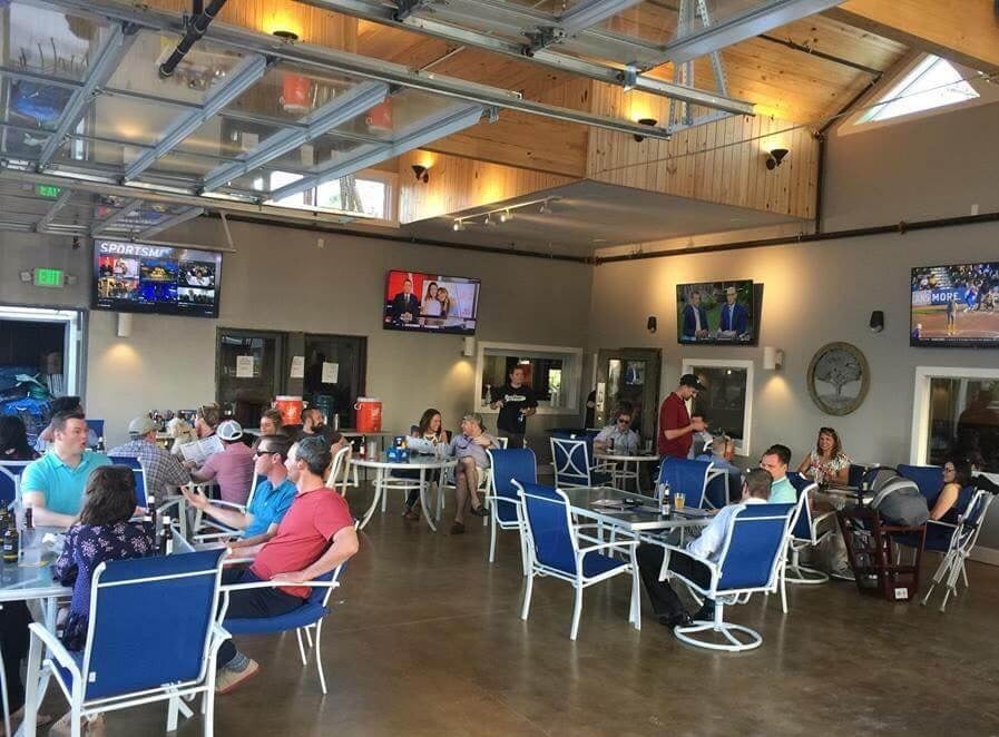 People sit at tables eating and drinking inside a casual restaurant with several TVs on the walls showing sports and news.