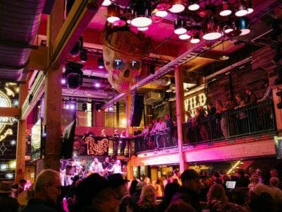 Indoor music venue in downtown Nashville with pink-purple lighting, people on two levels, a large decorative skull hanging from the ceiling, and neon signs in the background—perfect for a progressive party or unforgettable Nashville party experience.