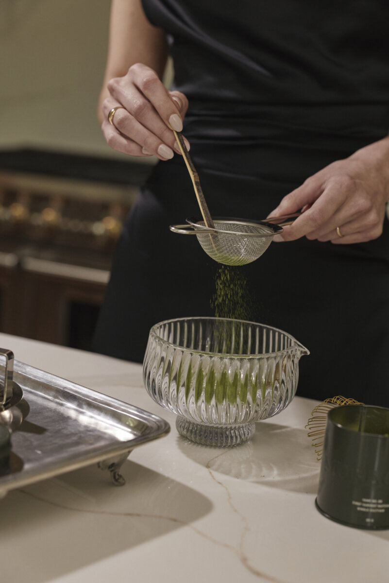 Meet the Sisters Behind Muracha: The South's New Must-Try Matcha - 6 A person sifts premium matcha green powder through a small strainer into a glass bowl on a kitchen counter, savoring the vibrant aroma of this South Muracha delight.