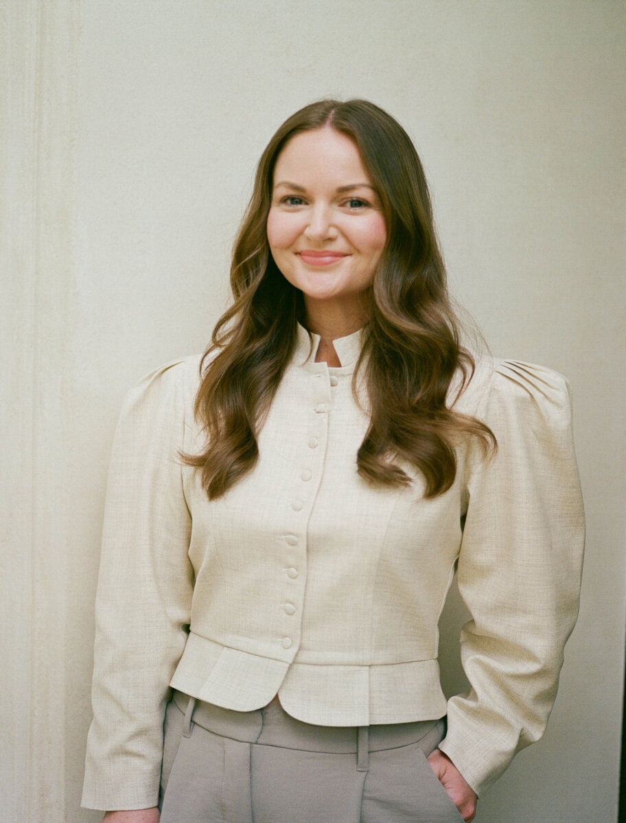Meet the Sisters Behind Muracha: The South's New Must-Try Matcha - 4 Woman with long brown hair stands against a plain light background, wearing a cream-colored buttoned jacket and gray pants, smiling slightly with hands by her sides.