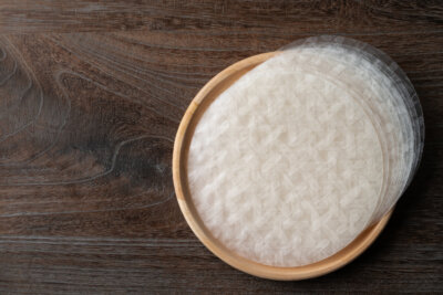 Round rice paper sheets, perfect for following the latest recipe trend, are stacked on a wooden plate and placed on a dark wooden surface.