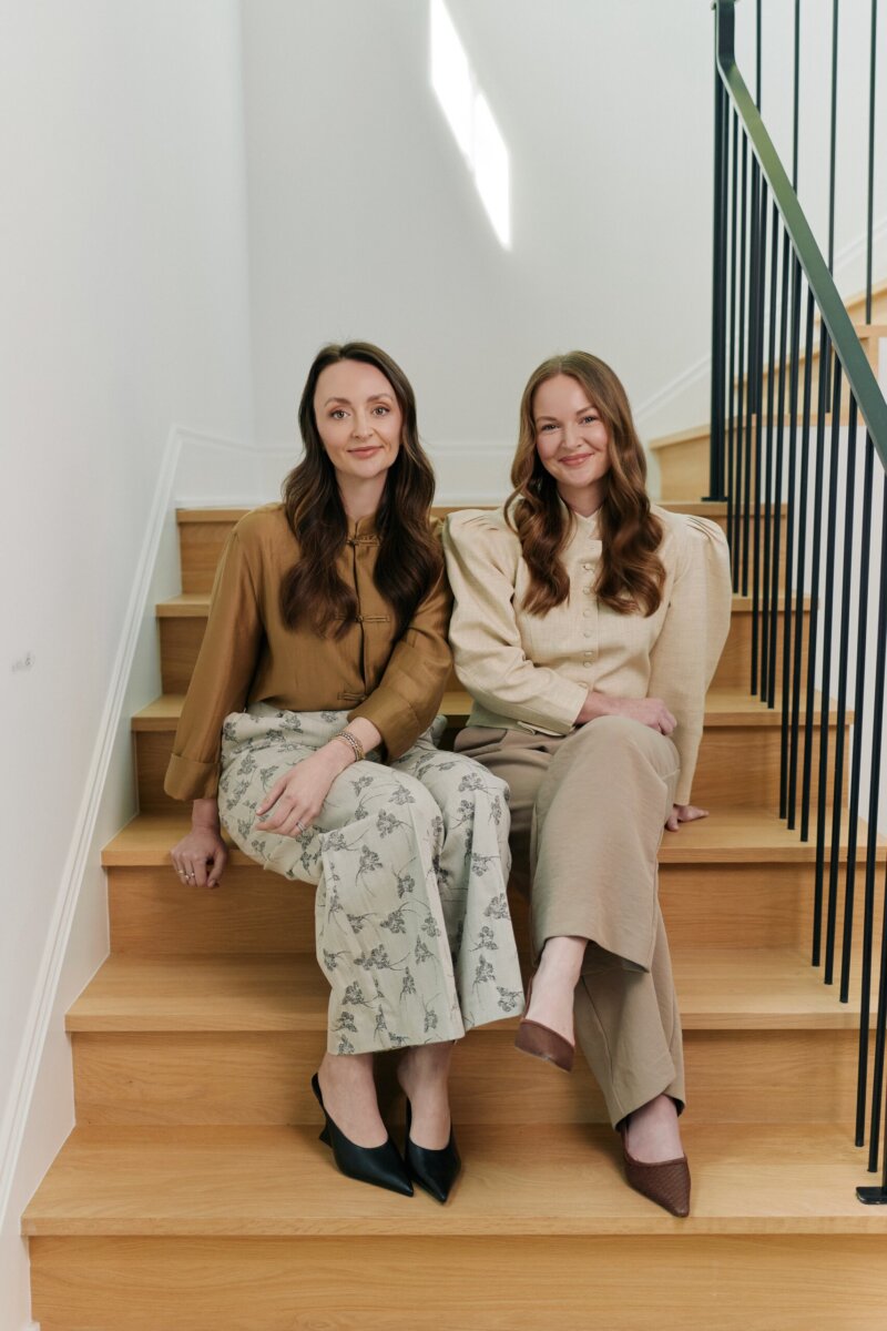 Meet the Sisters Behind Muracha: The South's New Must-Try Matcha - 2 Two sisters, sit side by side on wooden stairs indoors, both wearing neutral-toned blouses and pants, looking at the camera with relaxed expressions.