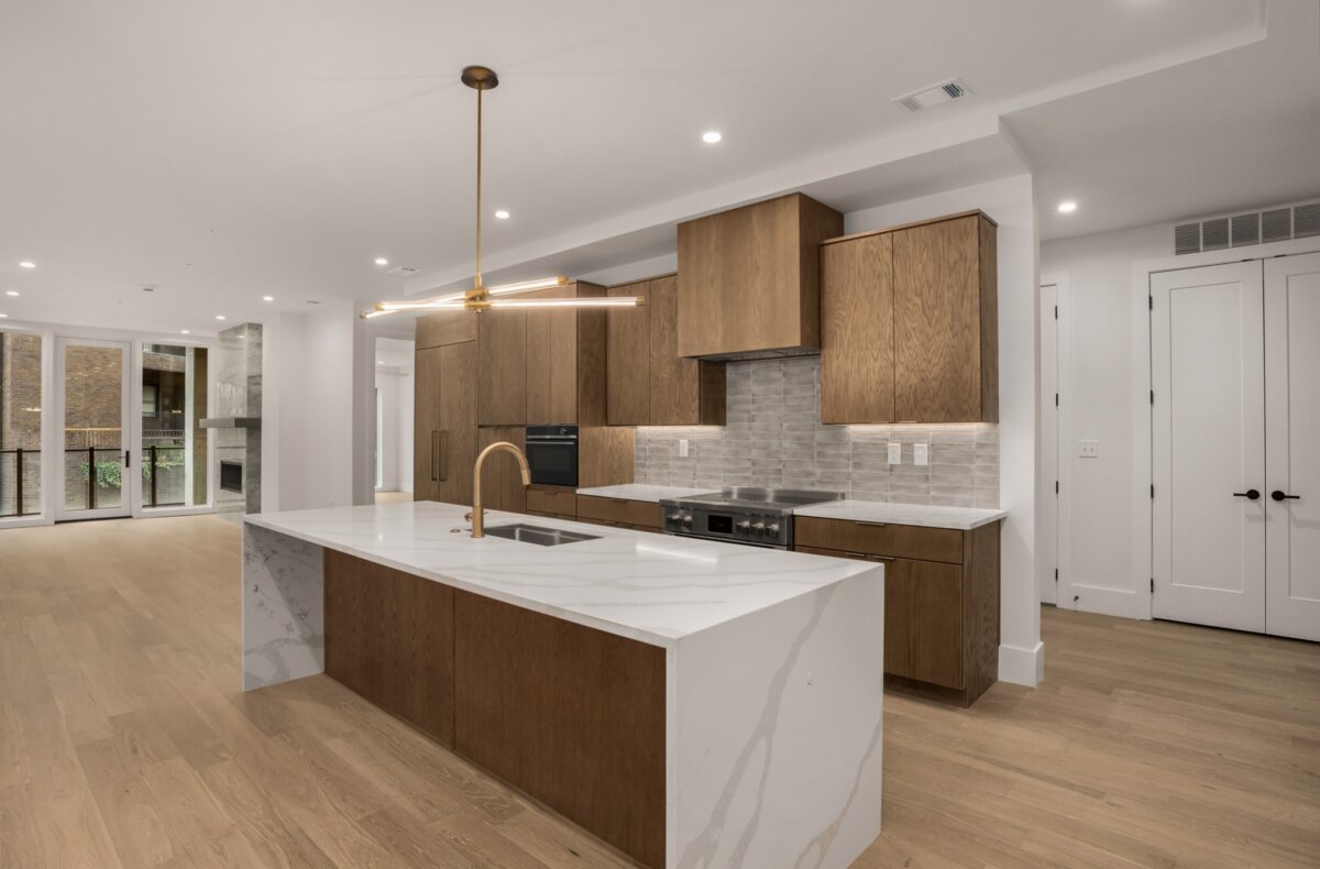 Modern kitchen with wood cabinets, marble island with sink, gold faucet, built-in oven, light wood floors, and large windows in the background—an exceptional feature of apartments at 321 31st Ave N in Nashville.