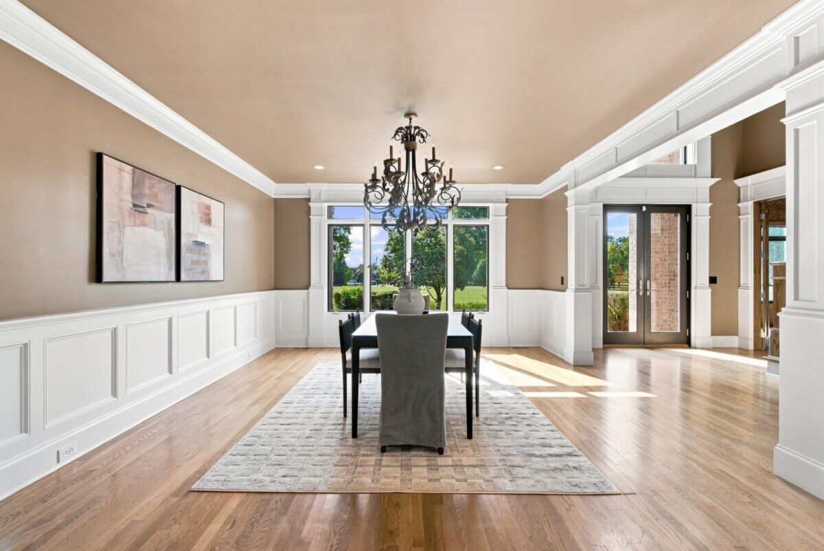 Modern dining room at 218 Steelson Way, Murfreesboro TN, featuring a rectangular table, six chairs, a decorative chandelier, large windows, neutral walls, and wood flooring. Natural light fills the space, and greenery is visible outside.