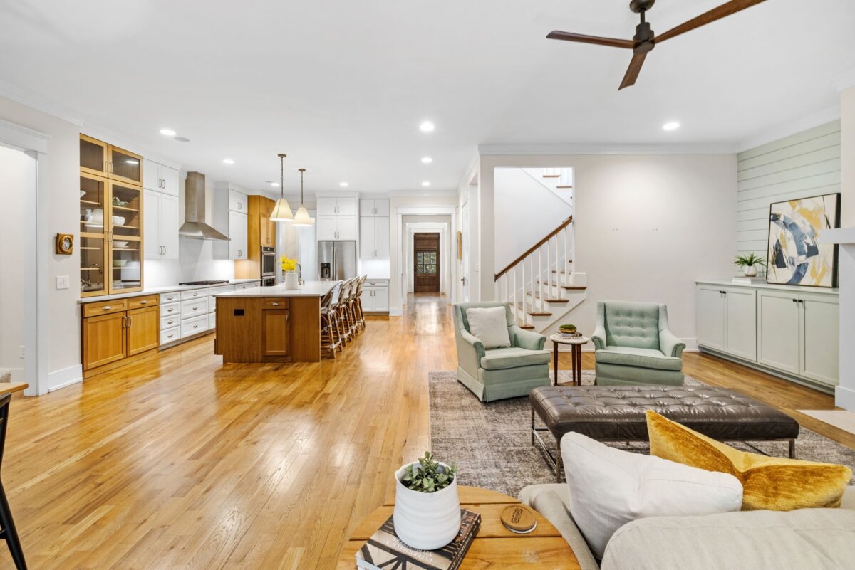Open-concept living area with hardwood floors, modern kitchen, large island, dining space, seating area, and staircase leading upstairs in the heart of 4000 Wallace Lane, Nashville TN. Neutral tones and recessed lighting throughout create a warm and inviting atmosphere.