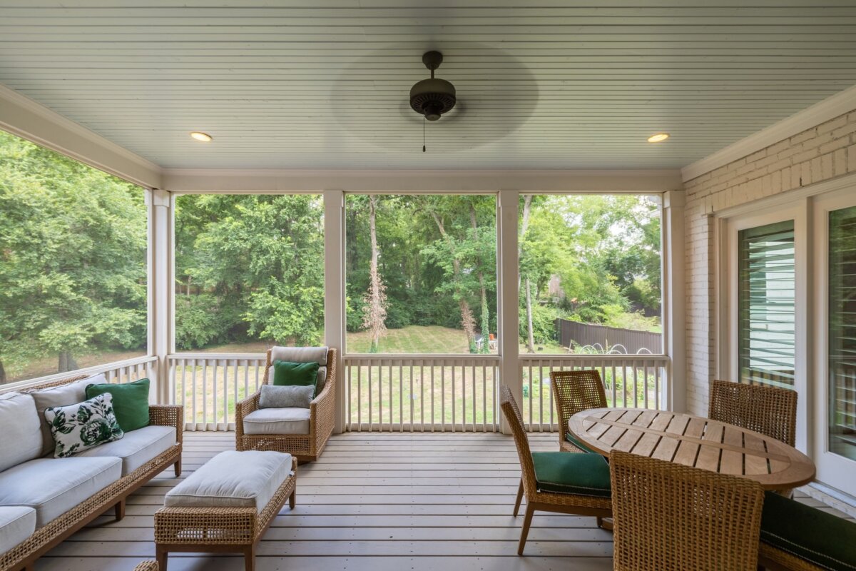 Screened-in porch with wicker furniture, a round wooden table with green cushions, a ceiling fan, and a view of the grassy backyard with trees at 4000 Wallace Lane in Nashville.