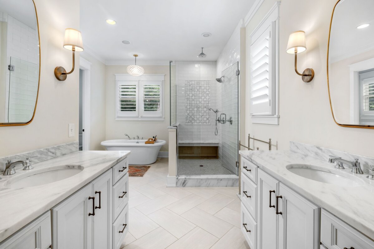 Modern bathroom at 4000 Wallace Lane, Nashville TN, featuring double sinks, marble countertops, wall sconces, a glass shower, freestanding tub, white cabinets, and a window with shutters.