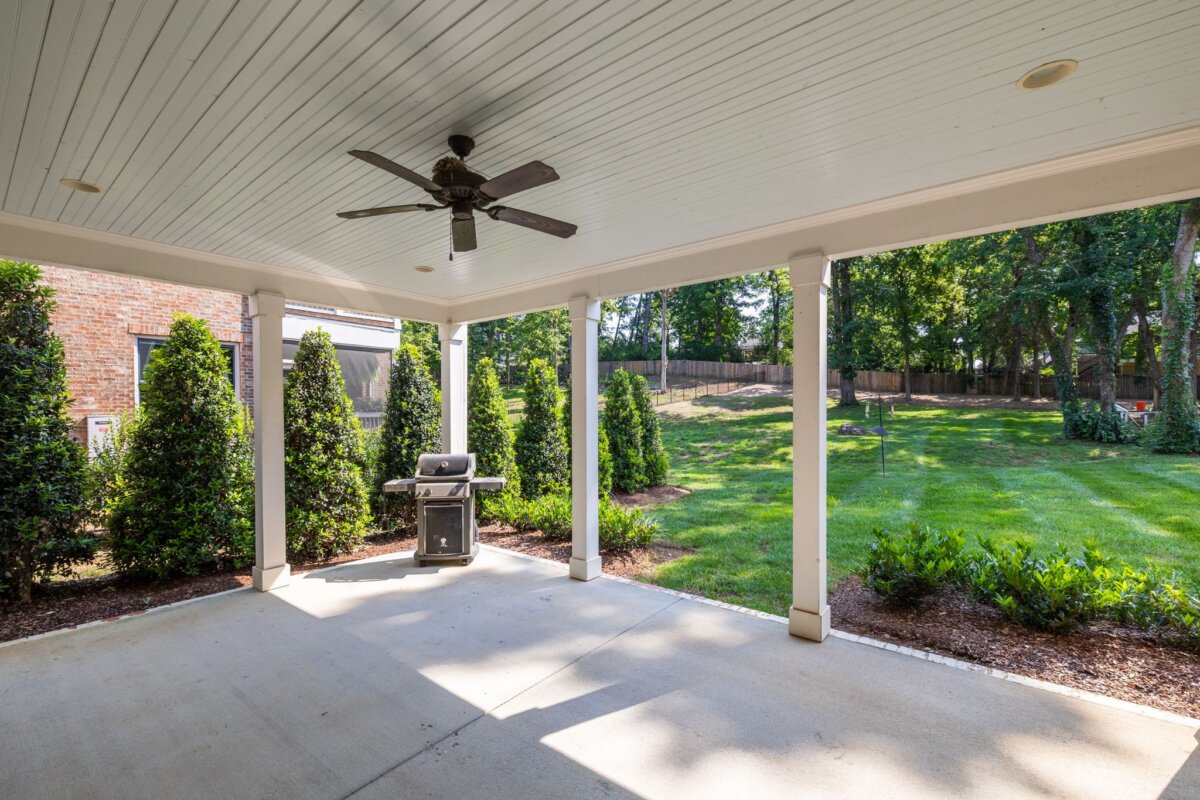 Covered patio with ceiling fan and grill at 4000 Wallace Lane, Nashville, overlooking a backyard with grass, shrubs, and trees bordered by a wooden fence.