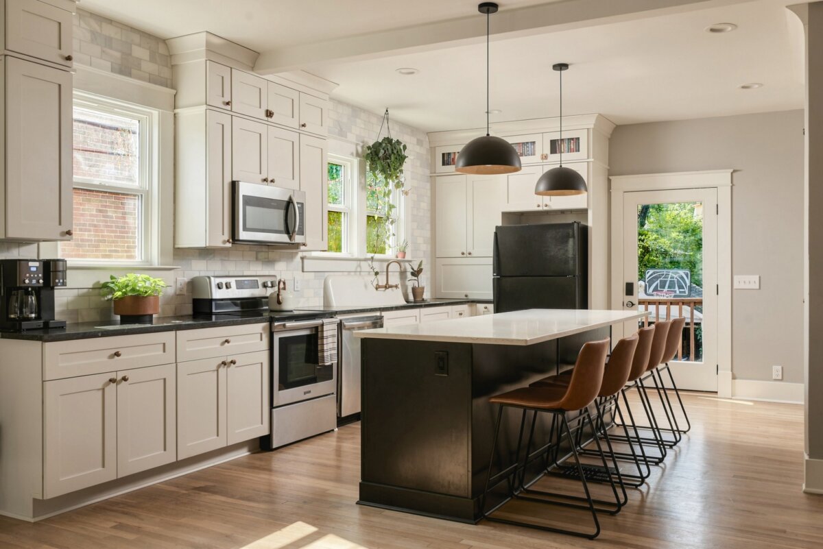 Modern kitchen with white cabinets, stainless steel appliances, black island with seating, pendant lights, and a door leading outside. Light wood floors and a window provide natural light in this stunning home at 2505 W Linden Ave, Nashville TN.