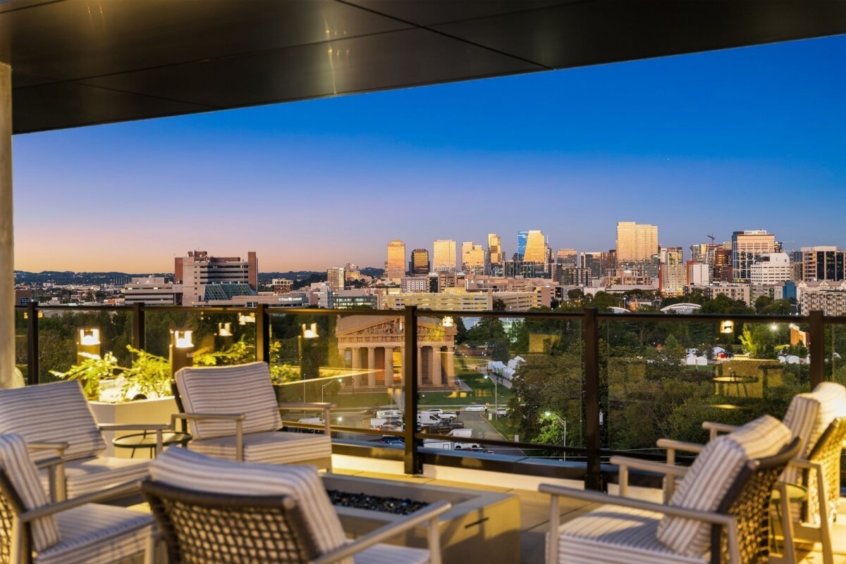 Rooftop patio with striped chairs overlooks the Nashville city skyline at sunset, with a classical-style building and greenery visible below at 321 31st Ave N, #310.