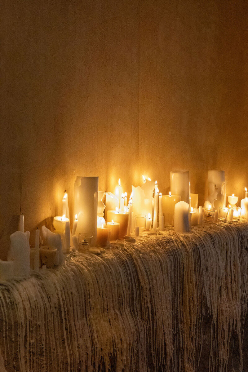 A row of various melted candles burning on a surface covered in wax drips, lighting up a dimly lit room with a warm glow—a scene that could inspire any interior designer or enthusiast of thoughtful interior design.