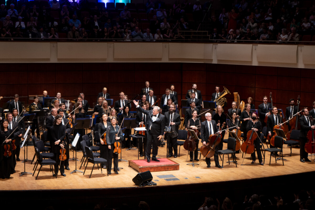 A symphony orchestra performs on stage, with the conductor gesturing to the audience during a visit to Birmingham.