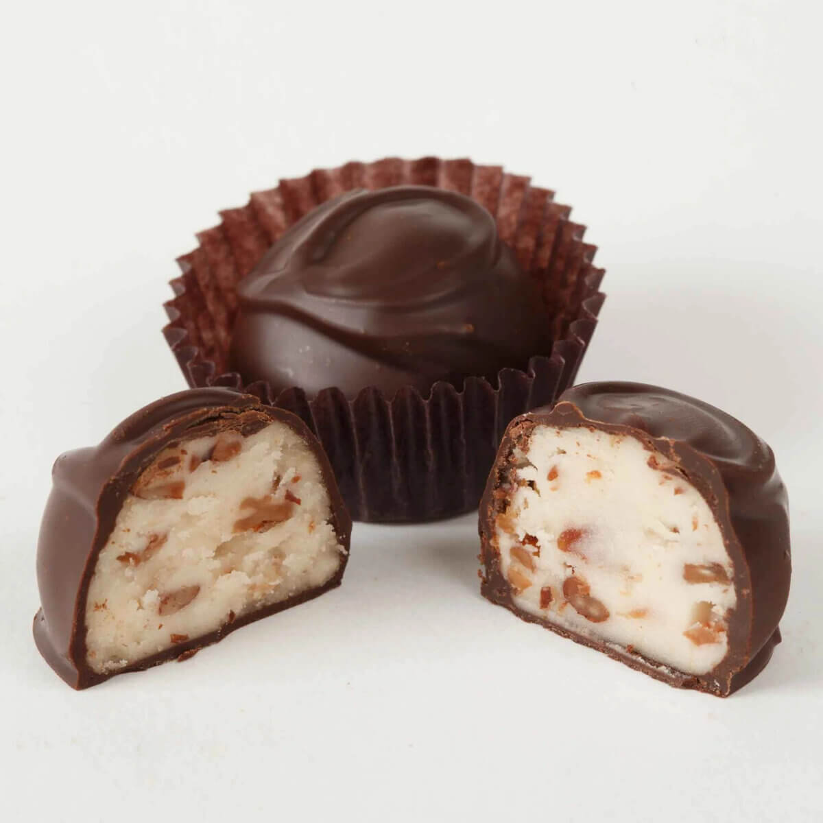 10 Grown-Up Halloween Candies We’re Keeping for Ourselves - 5 A whole and two halved chocolate candies with nut and cream filling are displayed on a white background, with one in a brown paper cup—a perfect example of grown-up Halloween candy for those seeking more sophisticated treats in their Halloween candy guide.