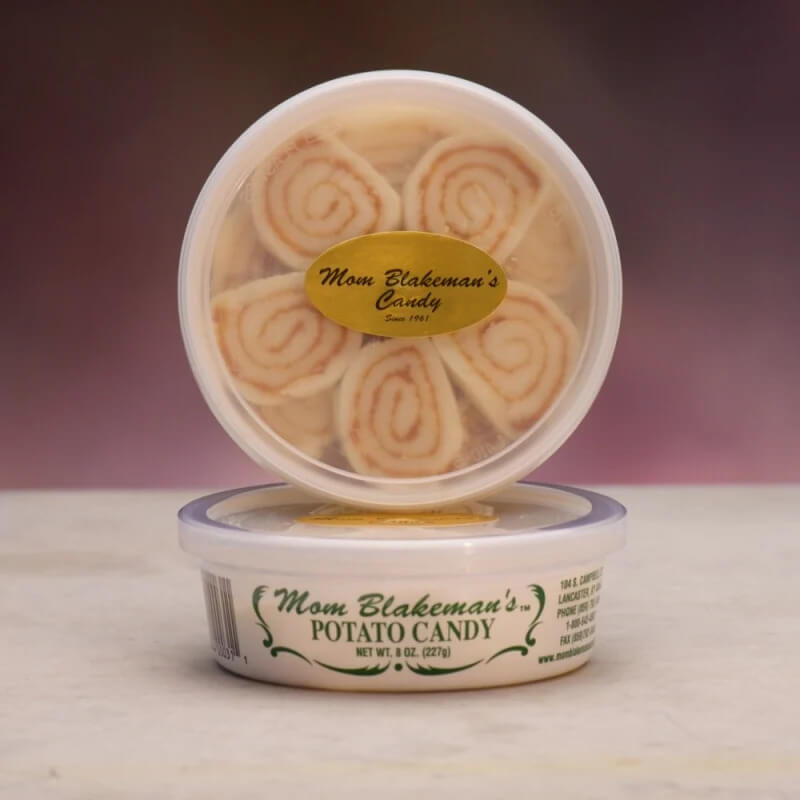 10 Grown-Up Halloween Candies We’re Keeping for Ourselves - 7 A round plastic container labeled “Mom Blakeman’s Potato Candy” filled with visible white and tan swirled candy pieces, placed on a light surface with a blurred background—an irresistible option for those seeking gourmet Halloween candy with a nostalgic twist.
