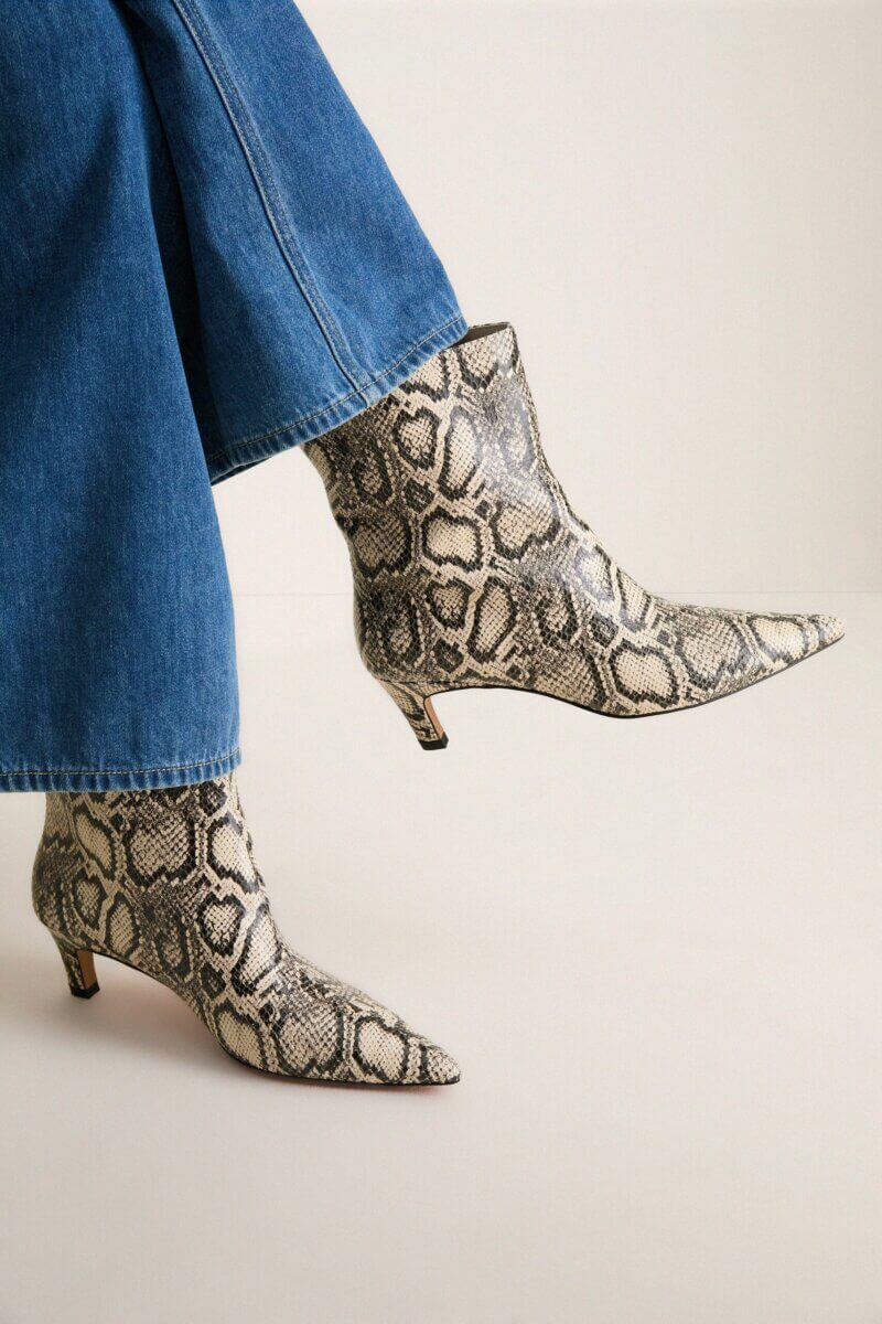 Fall Is Getting Wild: Animal Prints Are Back! - 16 A person wearing blue denim jeans and pointed-toe ankle boots with a gray and black snakeskin pattern, standing against a plain background—a perfect example of how to embrace Animal Print Trends for chic Fall Fashion.