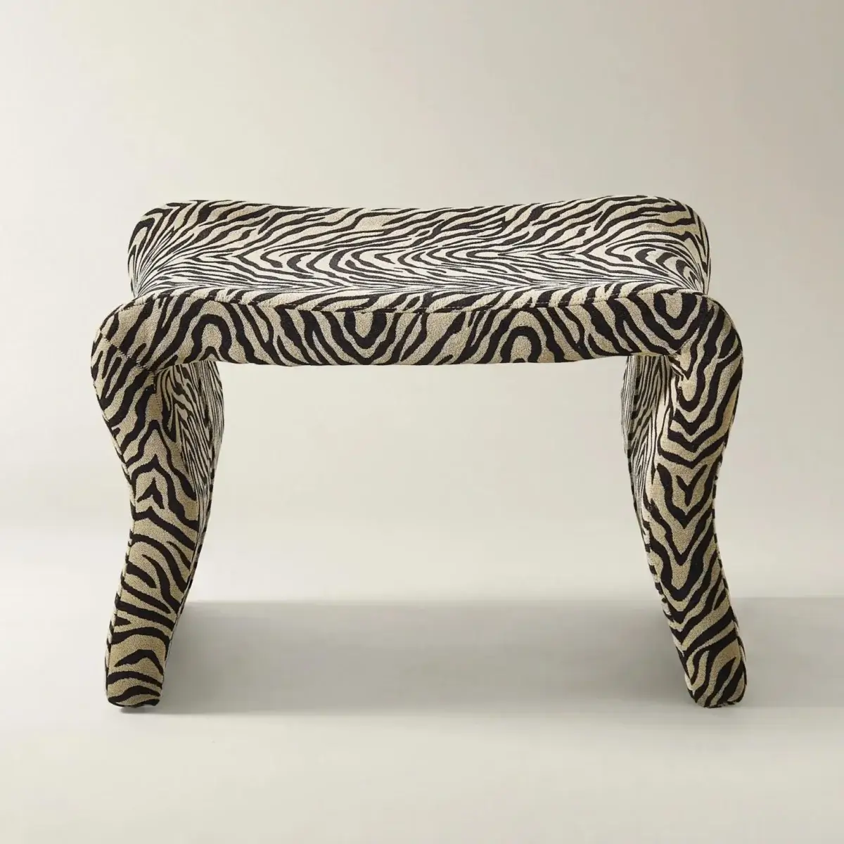 Fall Is Getting Wild: Animal Prints Are Back! - 27 A small bench or stool with curved legs, upholstered in fabric with a bold black and white zebra stripe pattern—a striking nod to animal prints—set against a plain background.