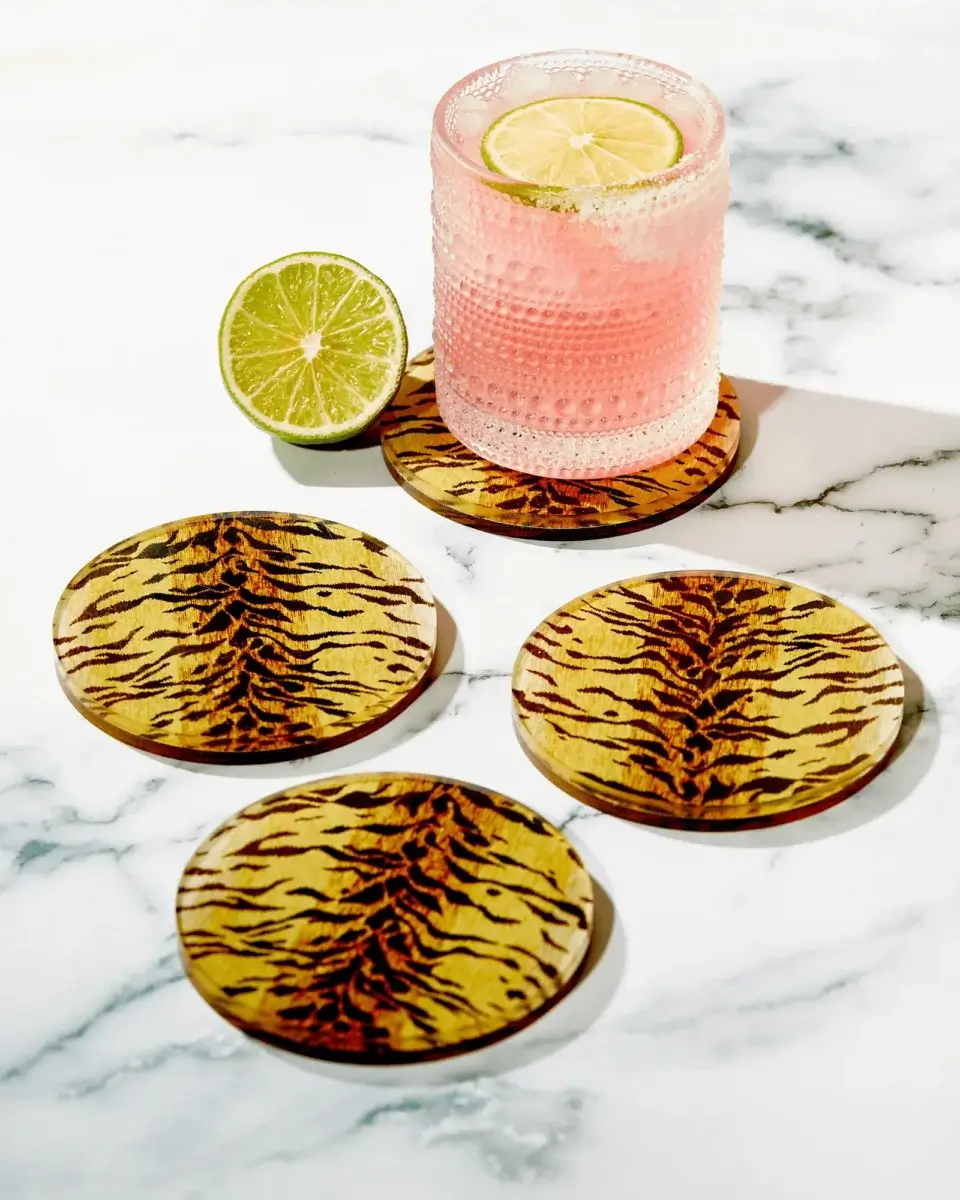 Fall Is Getting Wild: Animal Prints Are Back! - 31 A glass of pink drink with lime sits on a tiger print coaster, next to three matching coasters on a white marble surface—bringing a stylish touch that channels the bold energy of animal prints and hints at fall fashion inspiration.