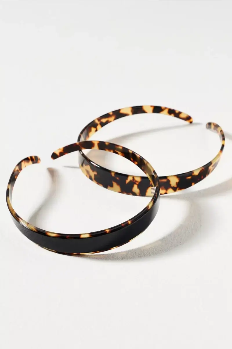 Fall Is Getting Wild: Animal Prints Are Back! - 26 Two plastic headbands with tortoiseshell patterns—one darker with mostly black, the other lighter with brown and tan patches—lie on a white surface, making them perfect accessories to embrace animal print trends for fall fashion.