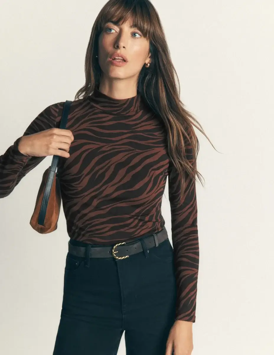 Fall Is Getting Wild: Animal Prints Are Back! - 2 Woman wearing a brown and black zebra print long-sleeve top, black jeans, and a black belt, holding a brown shoulder bag—a chic statement that perfectly showcases the bold elegance of animal prints in fall fashion.