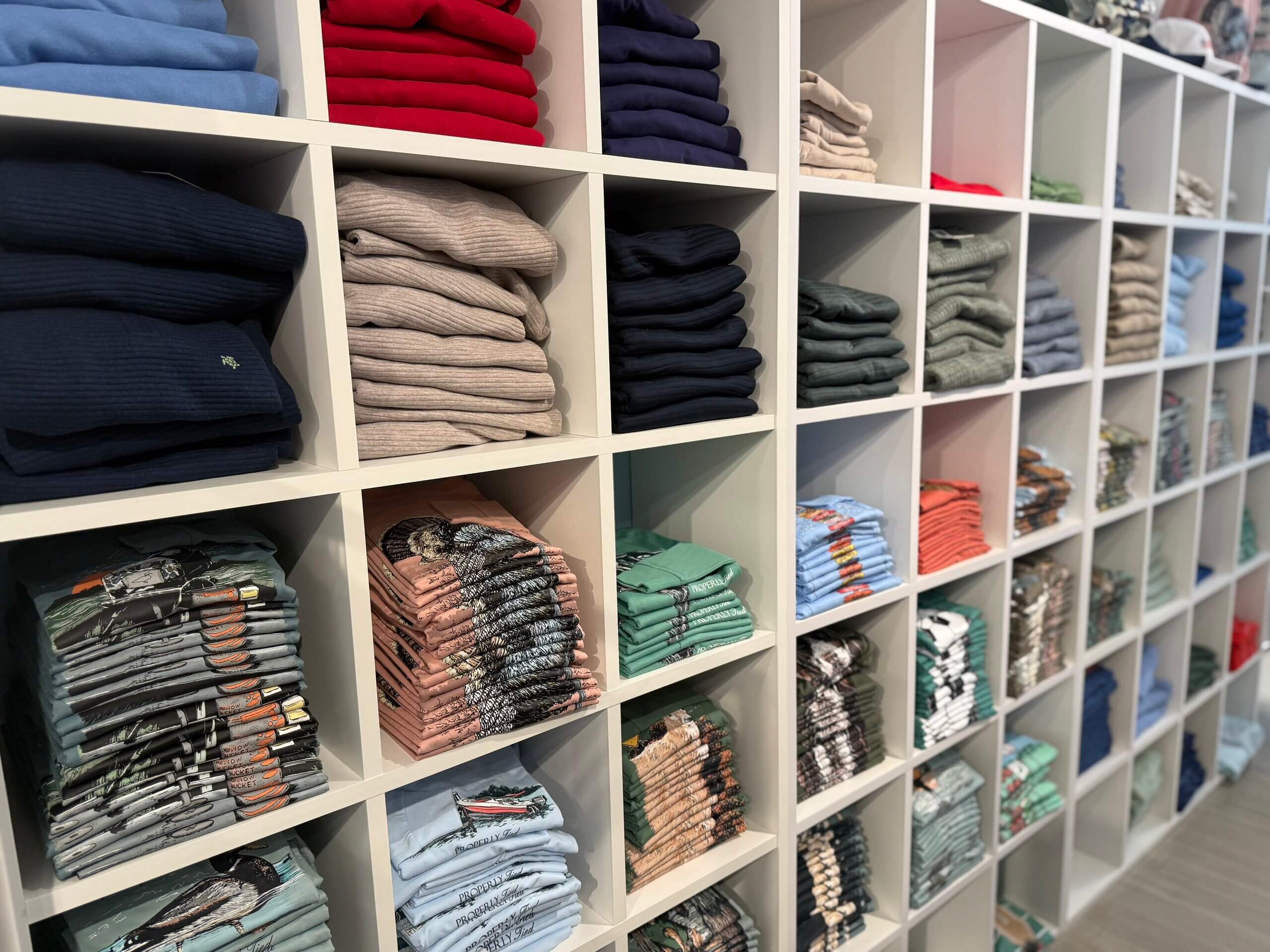 Shelves filled with neatly folded sweaters and t-shirts in various colors and patterns, organized by type and shade, create a vibrant display reminiscent of a Lili Pad collection—each layer thoughtfully arranged for effortless browsing.