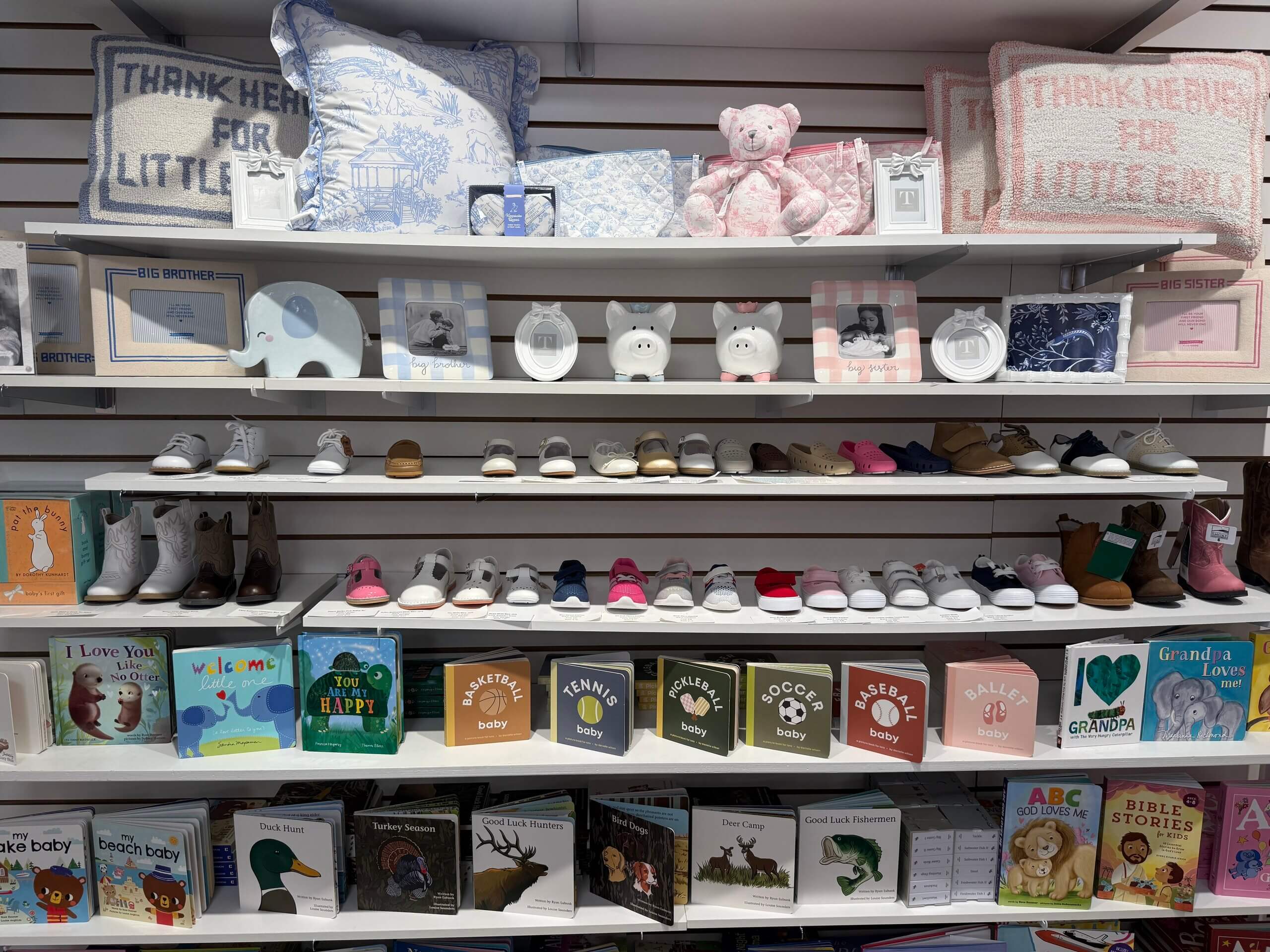 Shelves at Lili Pad display stuffed animals, pillows, baby photo frames, small shoes, and various children’s books in a charming store setting.