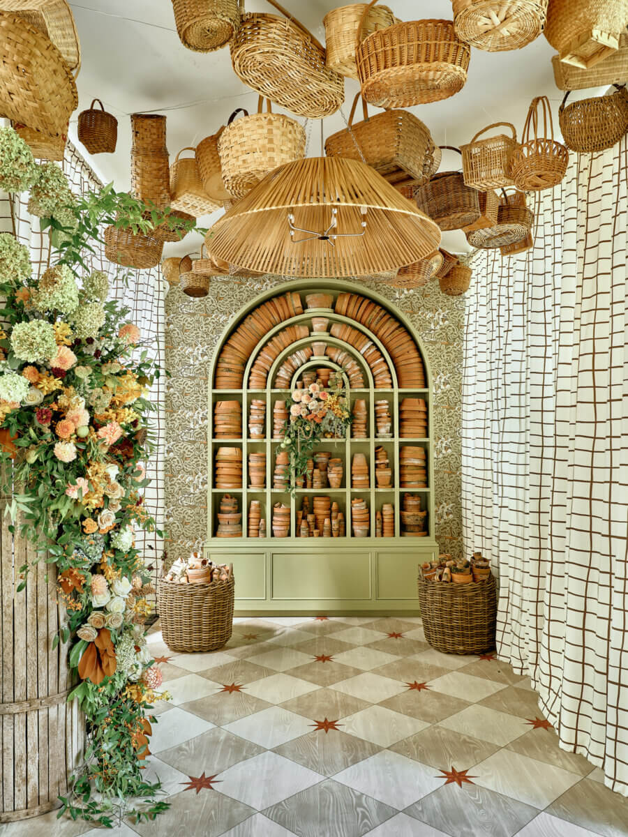 Room with patterned tile floor, floral arrangement, and shelves filled with terracotta pots; wicker baskets hang from the ceiling and are placed in large baskets on the floor—a scene reminiscent of displays at Birmingham Antiques or gatherings like Antiques at the Garden during Birmingham events.