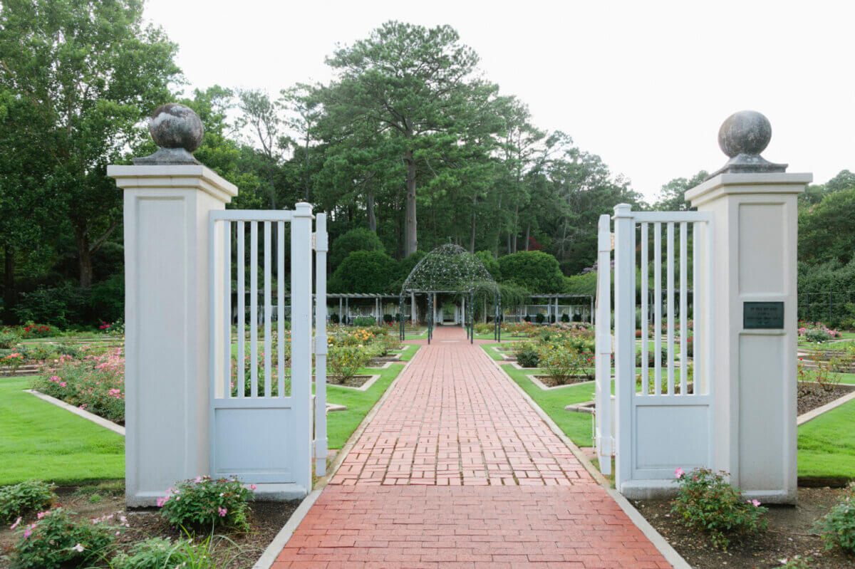 5 of Birmingham's Most Charming Walks - 5 Open iron gates reveal a red brick path leading through a manicured garden with trimmed lawns, flower beds, and a gazebo surrounded by tall trees in the background—perfect for enjoying charming walks reminiscent of the best Birmingham walking trails.