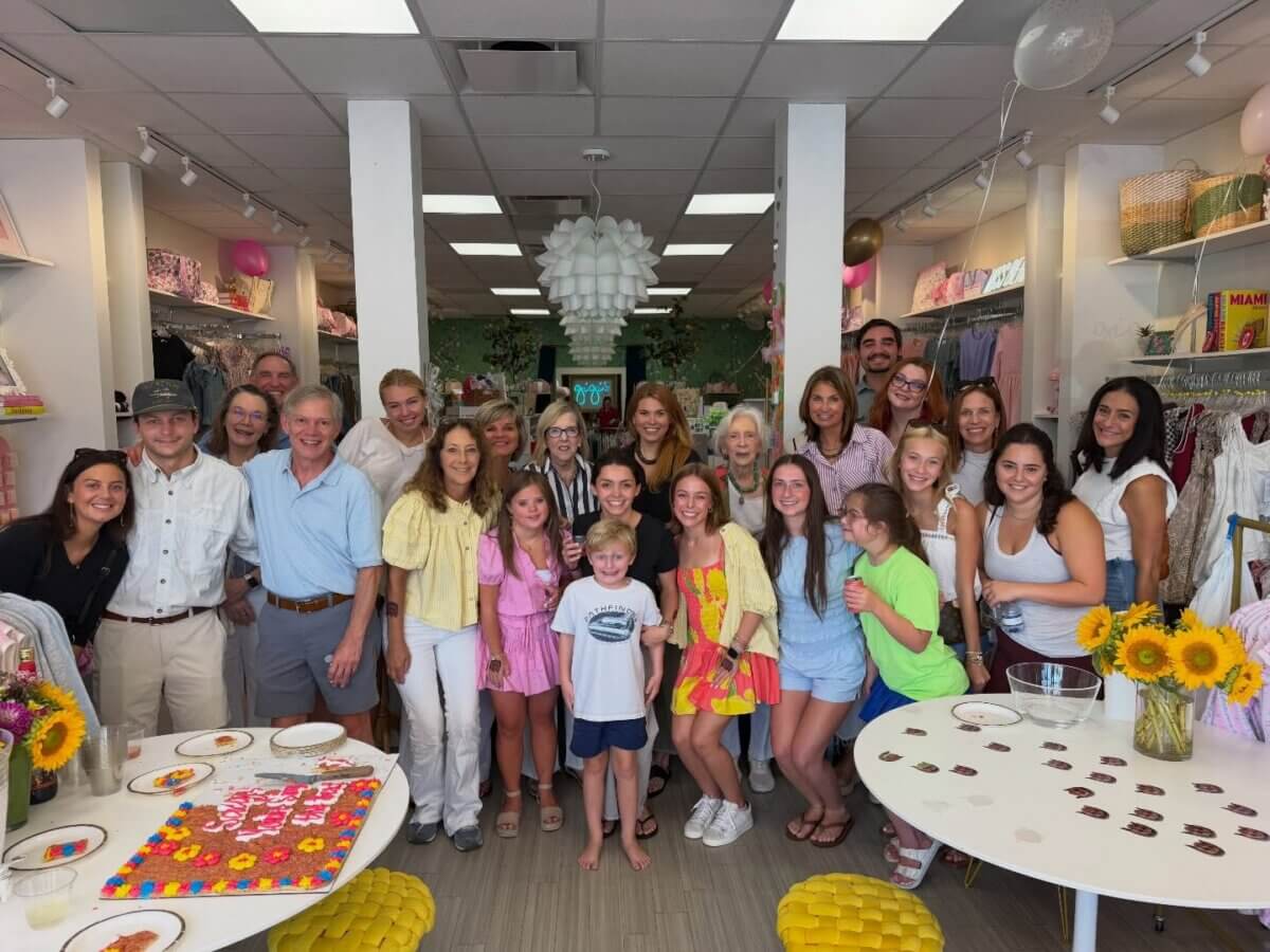A group of people of various ages pose together and smile inside Gigi’s, a brightly lit store decorated with sunflowers and colorful items—a true celebration of family legacy.