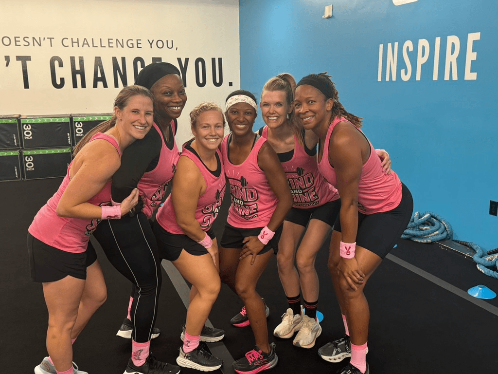 This BHAM Doctor Fights for Women's Lives Every Day - 6 Six women in matching pink workout outfits pose together and smile inside a gym, standing in front of motivational wall quotes, showcasing their commitment to research and advocacy for improving women’s lives.