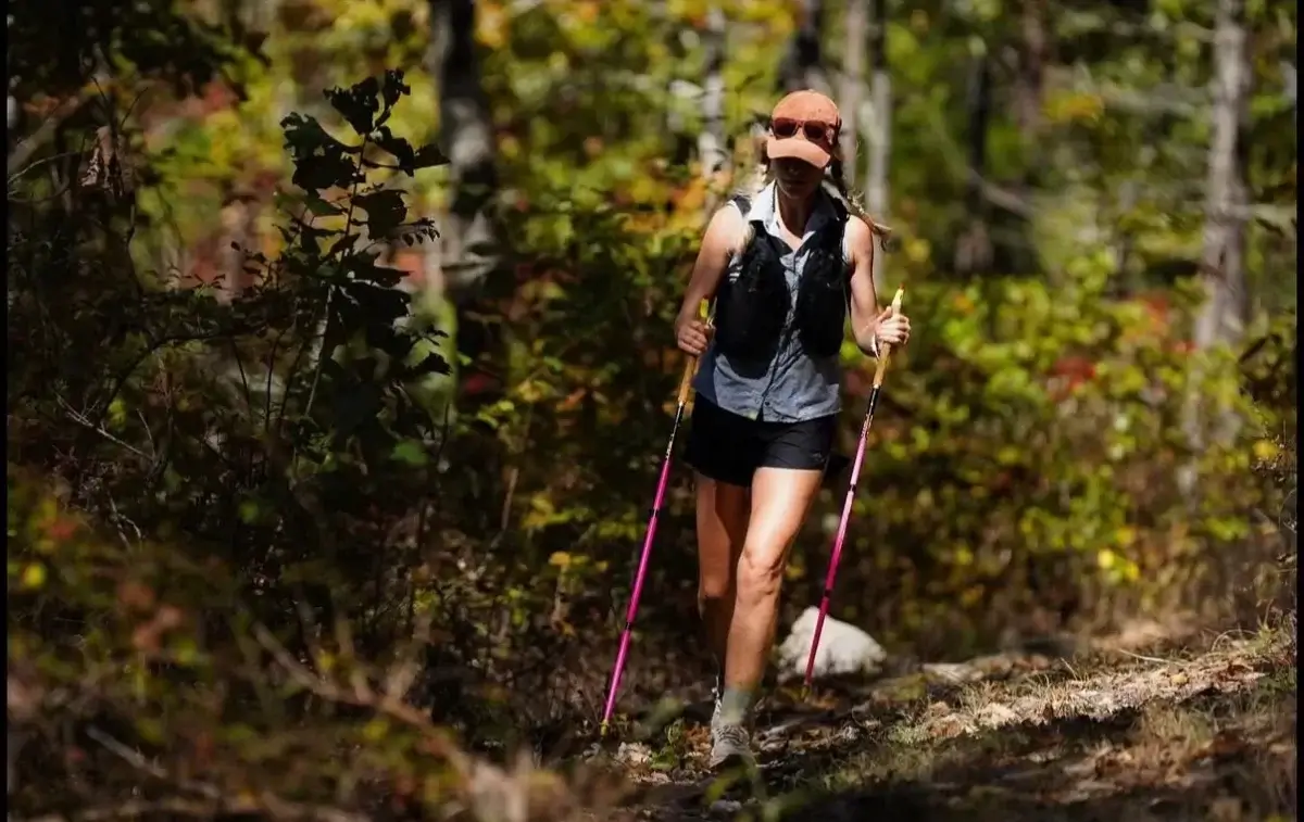 This BHAM Mom Ran 350 Miles in 5 Days - 4 Birmingham woman hiking on a forest trail with trekking poles, athletic gear, and backpack, surrounded by sunlit trees—part of her five days, 350 miles adventure.