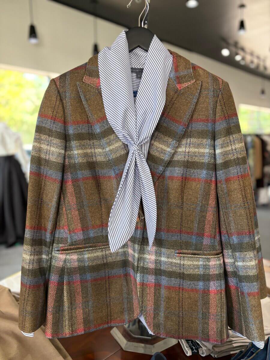Brown plaid blazer with red and blue stripes displayed on a hanger, paired with a striped scarf tied around the collar—a classic piece that embodies fall fashion and makes a standout addition to your collection of fall accessories.