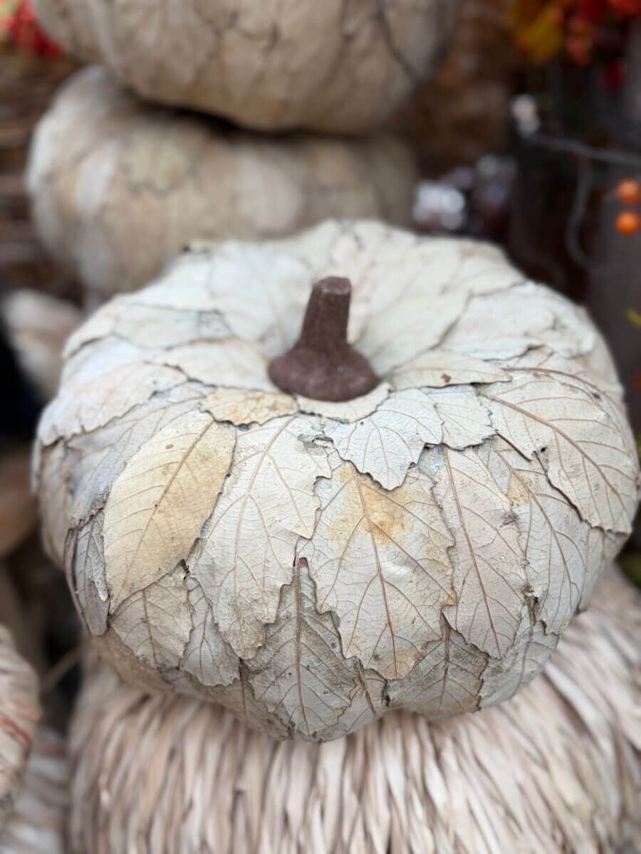 A decorative pumpkin made from dried leaves with a brown stem, displayed among other natural autumn decorations, brings an elegant touch of fall decor to any space.