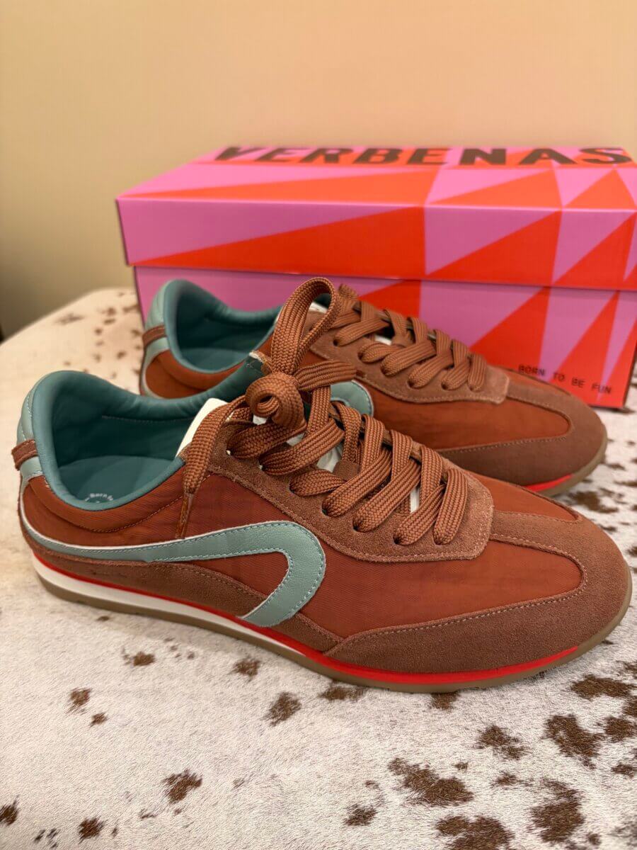 A pair of brown and teal sneakers with tan laces are placed in front of a pink and red Verbenas branded shoe box on a beige surface, making them the perfect addition to your fall fashion wardrobe.