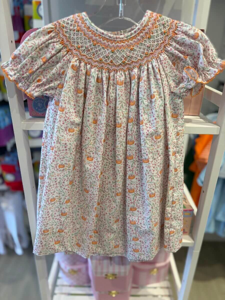 White floral smocked dress with short puff sleeves and orange embroidery, displayed on a hanger in a store—a perfect addition to your fall fashion wardrobe.
