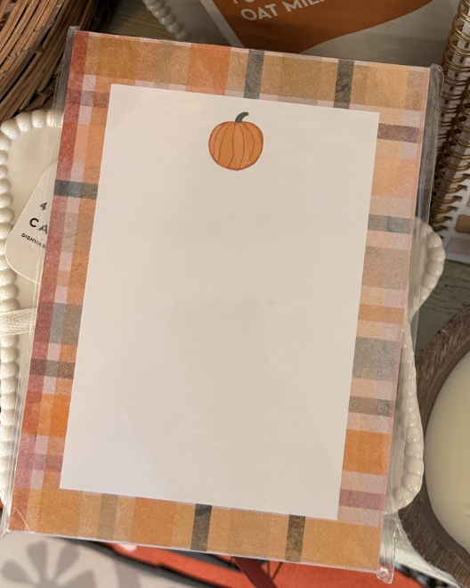 A notepad with a plaid orange border and a small pumpkin illustration at the top center, placed among decorative items, makes the perfect addition to your fall decor.