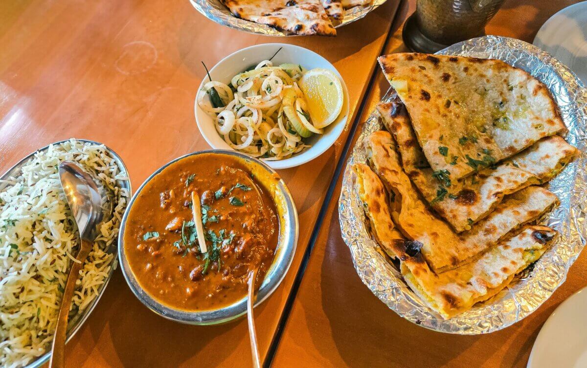 A table with naan, basmati rice, a bowl of curry garnished with cilantro, and a side of sliced onions and lemon invites you to Eat Your Way Around the World—from the flavors of Birmingham to vibrant global cuisine.