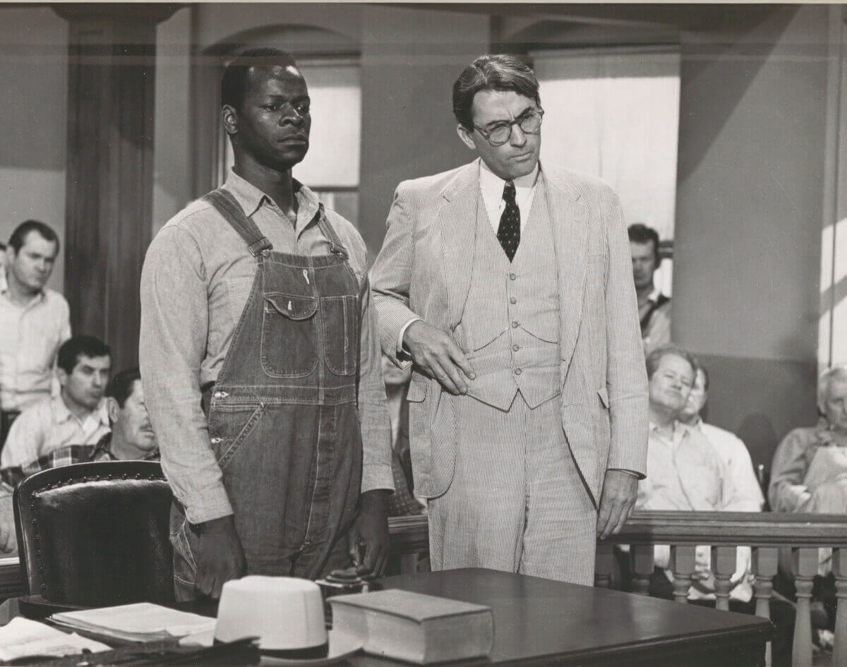 Tom Robinson stands beside Atticus Finch in a in a courtroom on the set of To Kill a Mockingbird.
