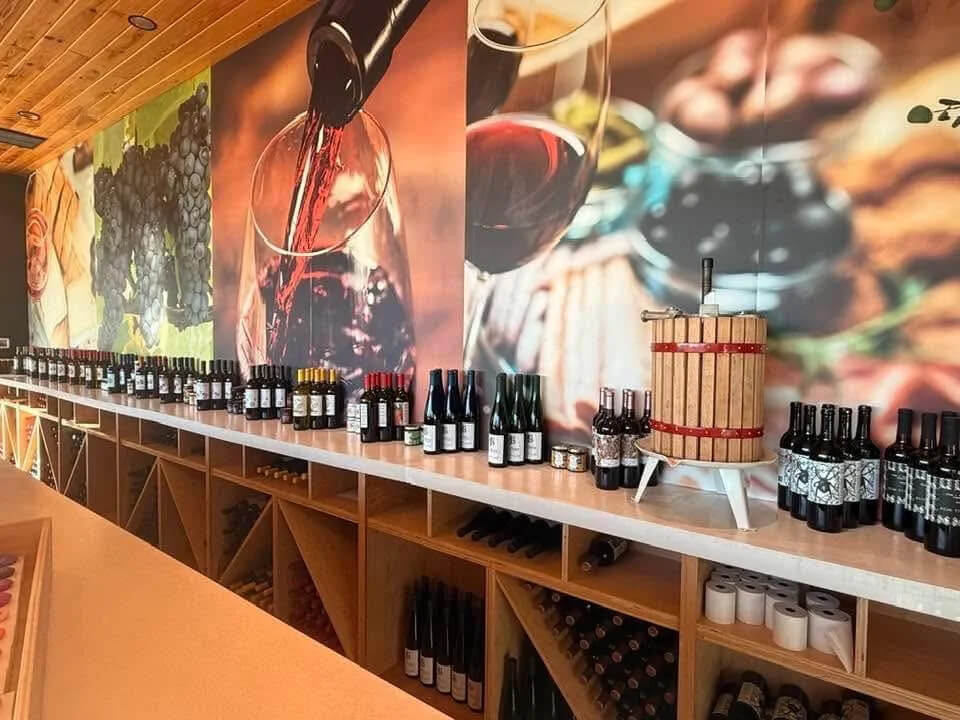 A wine shop interior with bottles displayed on a counter and in shelves below; large wine-themed murals decorate the wall, creating an ambiance reminiscent of some of the best wineries near Birmingham.