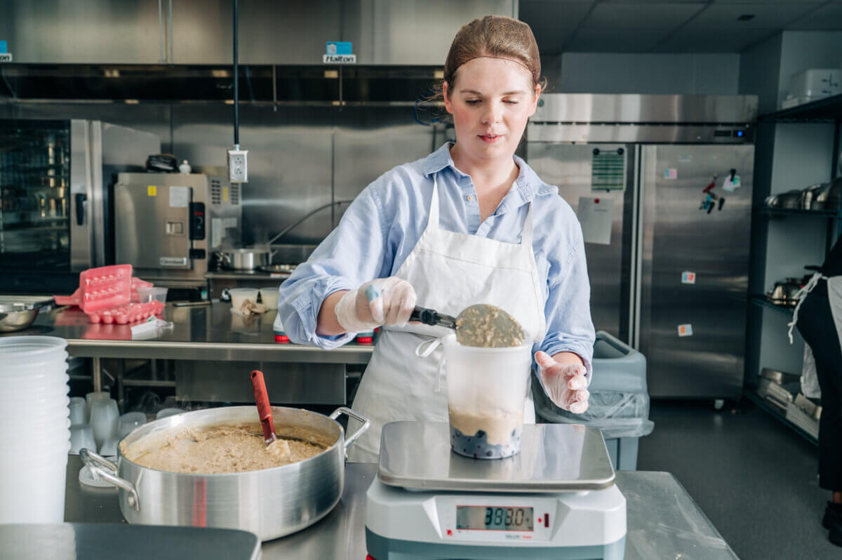 Pumpkin Is Not Just for Lattes — Supercharge Your Fall Smoothies and Salads! - 5 A person in a commercial kitchen scoops food from a pot into a container on a digital scale, following dietitian tips for portioning fall salads.