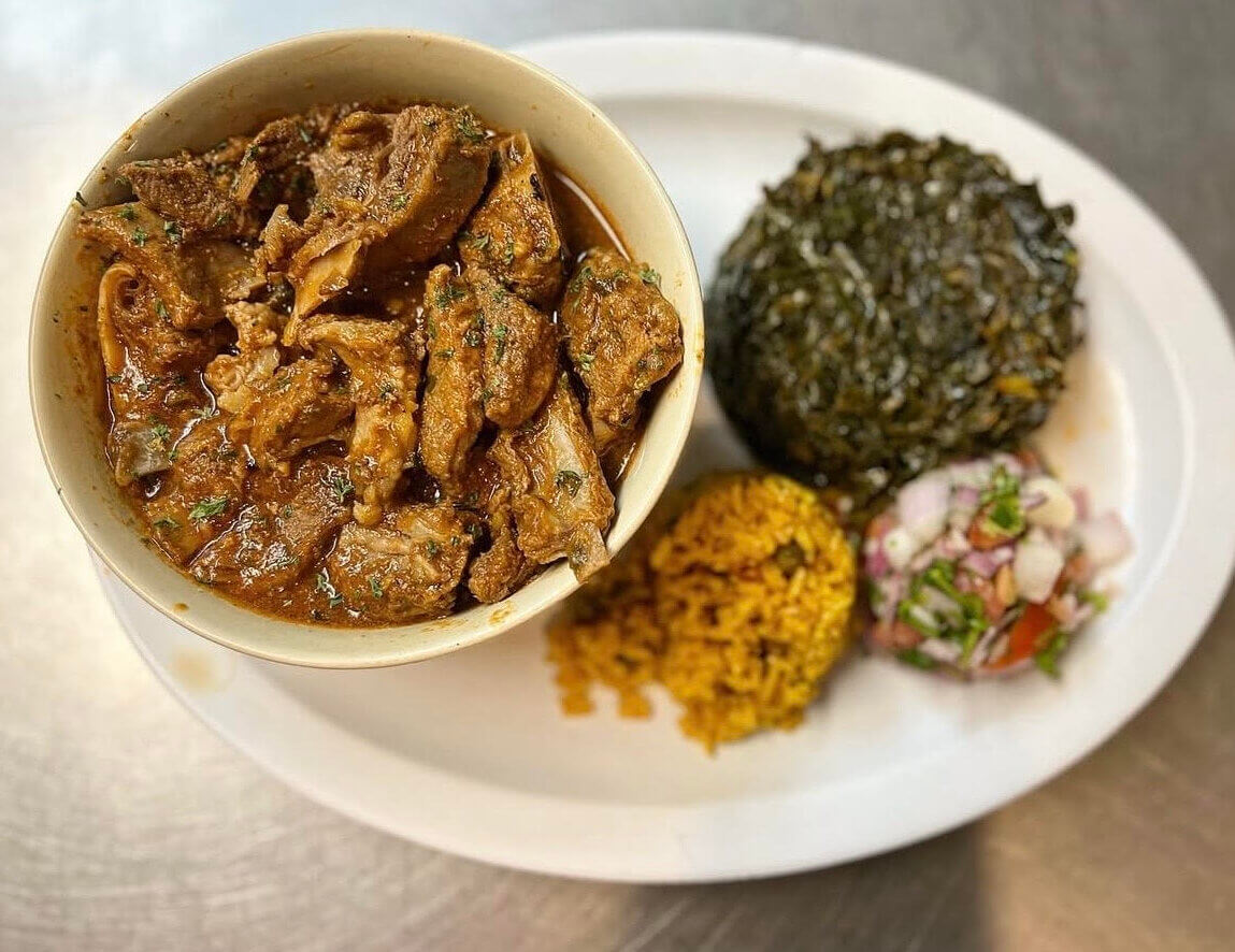 A plate with a bowl of spicy meat stew, a serving of green leafy vegetables, yellow rice, and a small portion of chopped tomato and onion salad—perfect for those looking to eat your way around the world with Birmingham’s vibrant international cuisine.