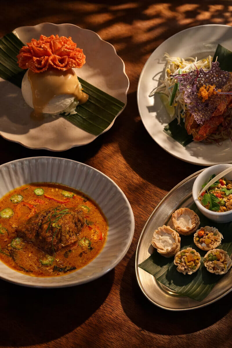 Four plates of Thai cuisine, including a curry dish, appetisers in crispy cups, a salad with colorful crisps, and a dessert topped with a spiral garnish, presented on a wooden table—an invitation to Eat Your Way through world cuisine right here in Birmingham.