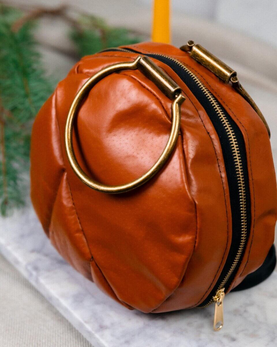 She Brings Bold Fashion, Cultural Heritage & Creativity to Memphis - 3 Round, brown leather Samilia Pelshak handbag with a large gold metal ring handle and zipper closure, placed on a marble surface with greenery in the background.