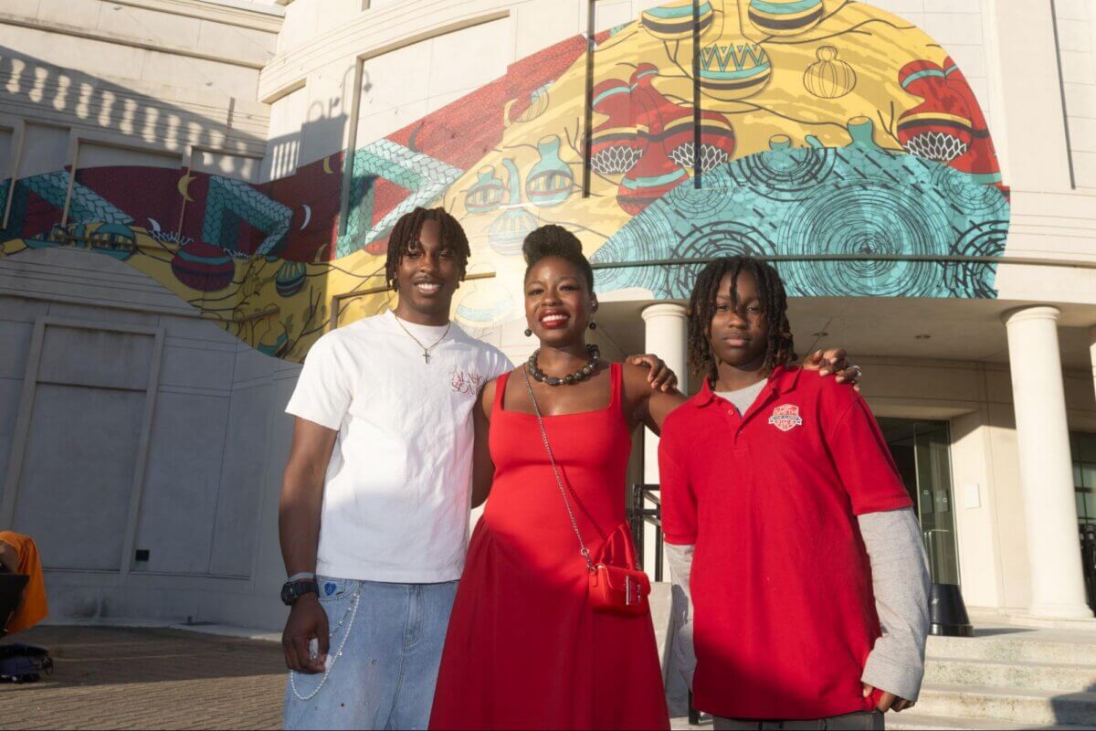 She Brings Bold Fashion, Cultural Heritage & Creativity to Memphis - 7 Three people, including Samilia Pelshak, pose in front of a colorful mural on a building exterior; two wear red shirts and one wears a red dress.
