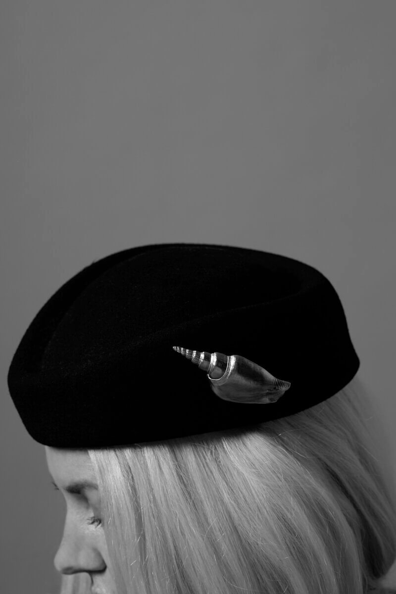 Gators, Magnolias, and Unicorn Horn Shells: Meet the New Orleans Designer Turning Southern Nature Into Jewelry - 4 A person with light hair wears a dark beret adorned with a decorative seashell pin, shown in black and white against a plain background.
