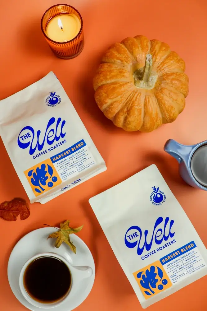 17 Fall-Ready Nashville FINDS: Cozy Layers, Beauty & Spooky Season Style - 15 Two bags of The Well Coffee Roasters Harvest Blend, a pumpkin, candle, black coffee, and milk pitcher on an orange surface—perfect Nashville finds for October.